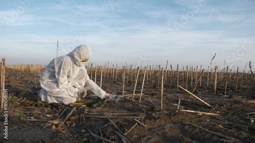 Slow motion footage of ecology specialists in white protection clothes observing and analyzing contaminated landscape, entering data on smartphone, collecting soil samples