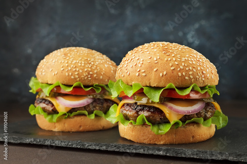 Homemad fast food: two burgers with beef, cheddar, lettuce, onion ang tomato on the slate board.