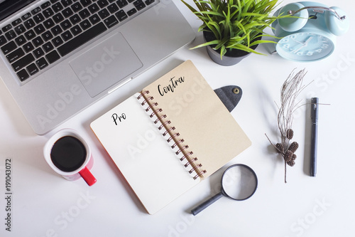 Laptop,spectacle,pen,dried flowers,coffee and a note book written with text PRO and CONTRA on white office table.Creative office table lay out. photo