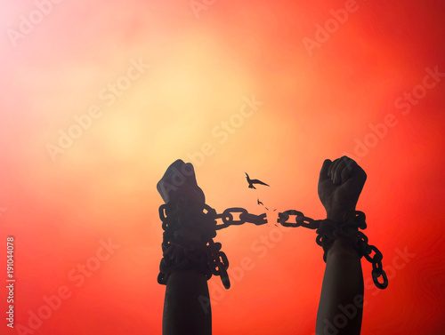 International day for the remembrance of the slave trade and its abolition concept: Silhouette human hands raising and broken chains on blurred red sunset background
