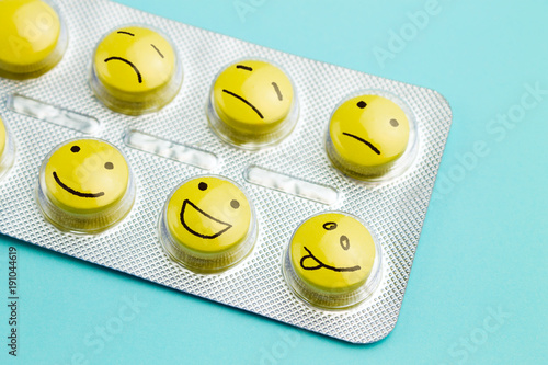 Yellow pills and funny faces in a blister on a blue background. The concept of antidepressants and healing photo