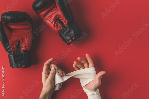 cropped shot of boxer covering up hands in elastic bandage before fight on red surface