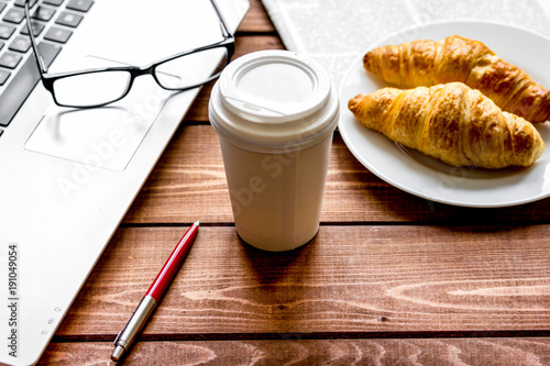 Business lunch with croissant and laptop on wooden desk photo