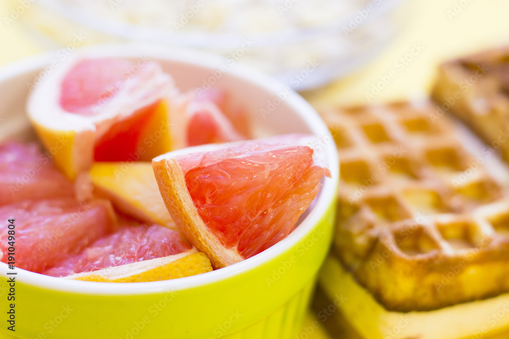 Delicious breakfast: fresh waffles and a bowl of sliced grapefruit on a yellow background with copy space