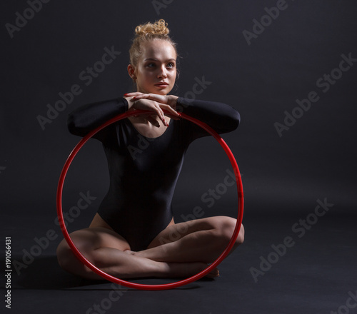 Portrait of young beautiful gymnast with a red wrap on a dark background.