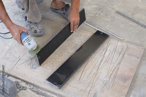 Worker cutting floor tiles with angle grinder at construction site