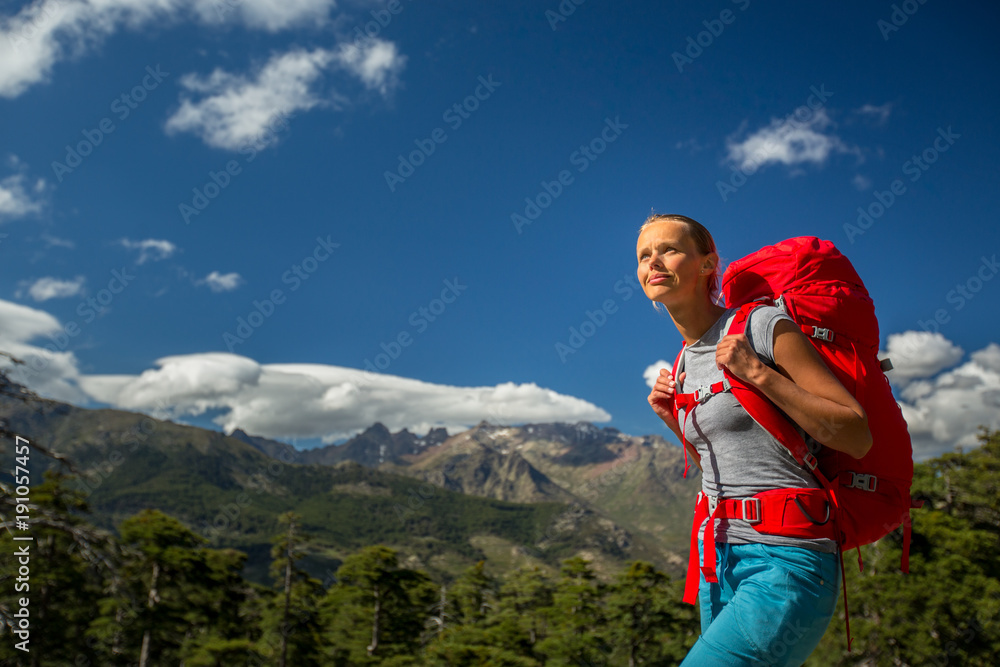 Pretty, female hiker in high mountains with her giant backpack, getting ready for some hiking