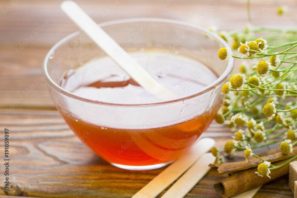 Set of sugaring essentials with natural honey, cinnamon sticks, and camomile on a natural dark wooden background Set of sugaring essentials with natural honey, cinnamon sticks, and camomile on a natural dark wooden background