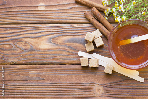 Dark natural wooden background with spa essentials: honey, cinnamon sticks, camomile and brown sugar cubes