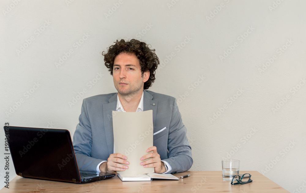 Young Caucasian businessman holding a blank sheet in front of empty clear wall Young Caucasian businessman holding a blank sheet in front of empty clear wall