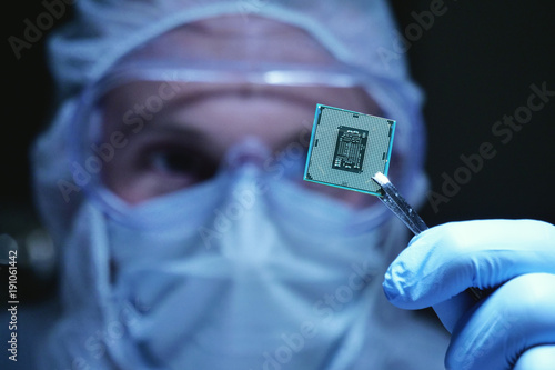 An Ultra Modern Electronic Manufacturing Factory Design Engineer in Sterile Coverall Holds Microchip with symbols in futuristic holography photo