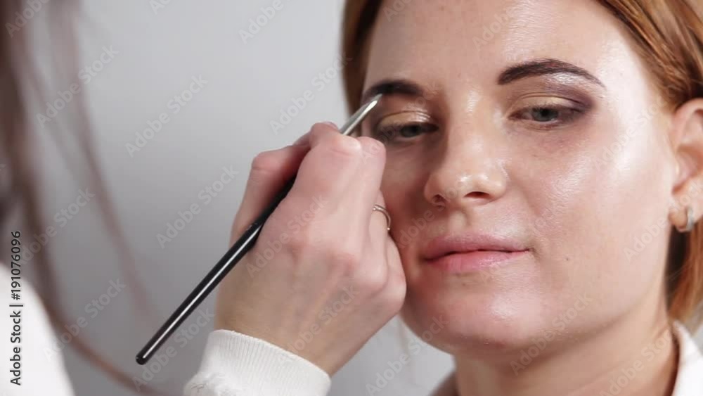 portrait of a young and beautiful woman who is waiting for the end of make-up, a professional make-up artist puts a dark color on the eyebrows of a woman, an artist uses a pencil portrait of a young and beautiful woman who is waiting for the end of make-up, a professional make-up artist puts a dark color on the eyebrows of a woman, an artist uses a pencil