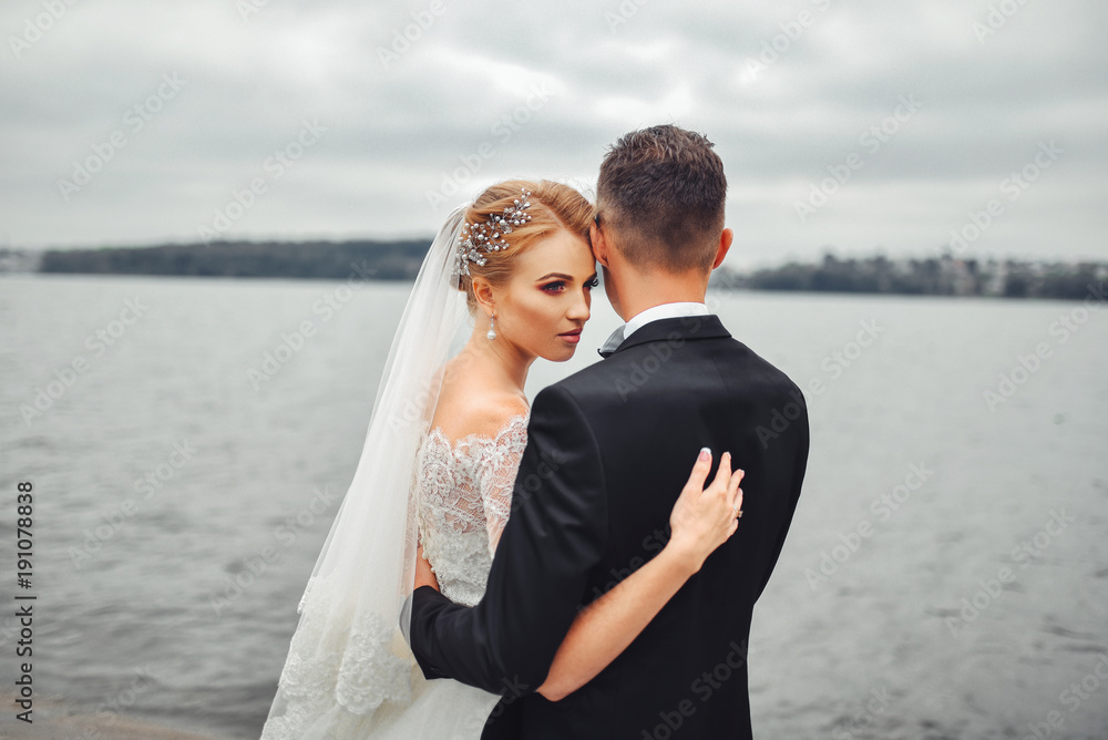 Obraz premium Posing for the camera. Young wedding couple. Romantic Married Couple. The bride and groom stand leaning against each other. The bride with a wreath of and a bouquet. Redhed bride haired young