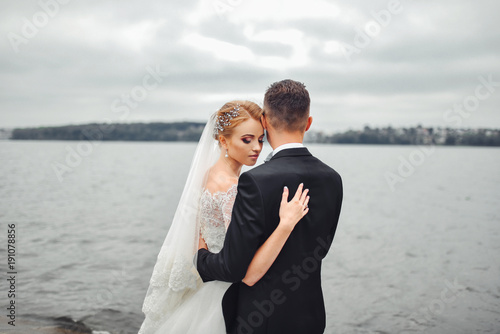 Posing for the camera. Young wedding couple. Romantic Married Couple. The bride and groom stand leaning against each other. The bride with a wreath of and a bouquet. ?edhed bride haired young