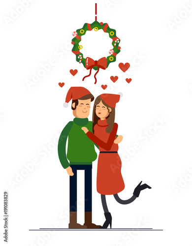 Couple of young people on Christmas Day kissing under the mistletoe wreath. Husband and wife celebrate winter holiday. Young family standing together holding each other.