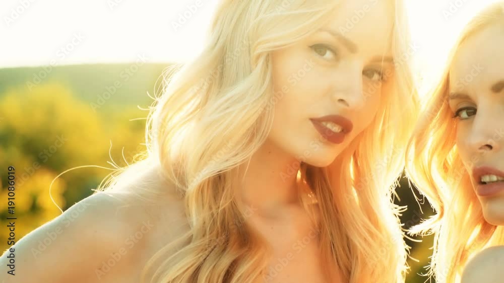girls or twin women, lesbian girlfriends, with long, blond hair, in fashionable, white sweaters air kissing on sunny day on natural background. Homosexual couple in love girls or twin women, lesbian girlfriends, with long, blond hair, in fashionable, white sweaters air kissing on sunny day on natural background. Homosexual couple in love