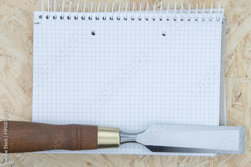 A professional chisel on a light wooden background, with a paper notebook