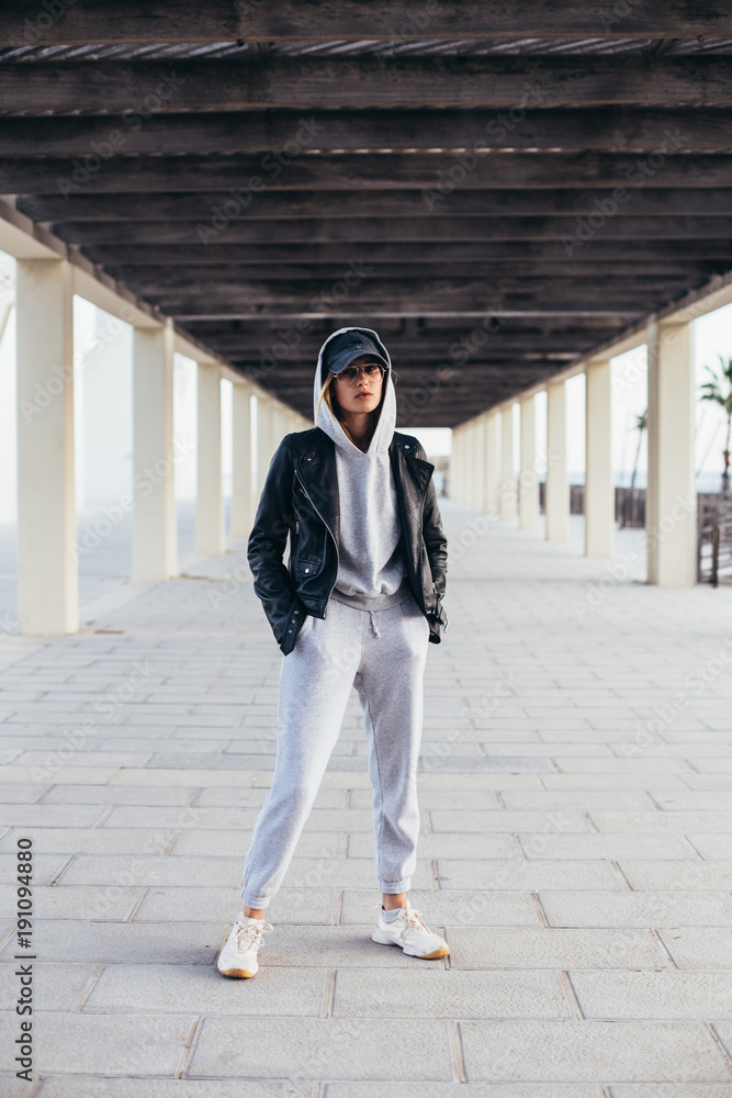 Cool and hip young female in grey fashionable tracksuit, sweatpants and  hoodie poses for camera during fashion photoshoot, urban street style for  social media or fashion outfit blog Stock Photo | Adobe