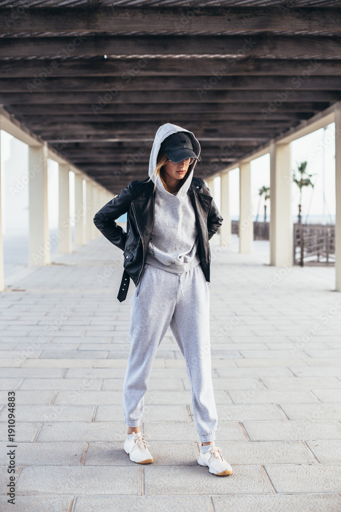 Cool and hip young female in grey fashionable tracksuit, sweatpants and  hoodie poses for camera during fashion photoshoot, urban street style for  social media or fashion outfit blog Stock Photo