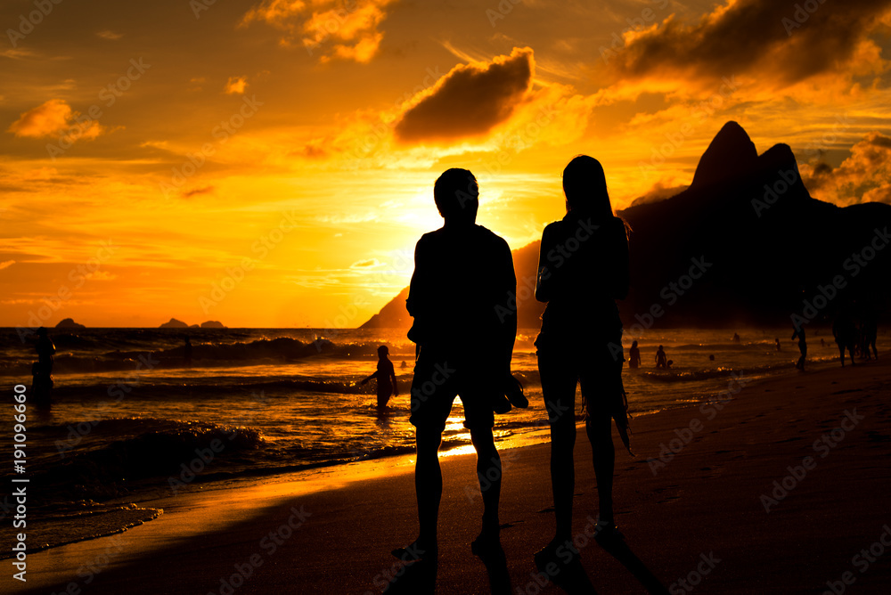 Silhouette of a Couple Walking in Ipanema Beach in Rio de Janeiro by Sunset with Mountains in Background