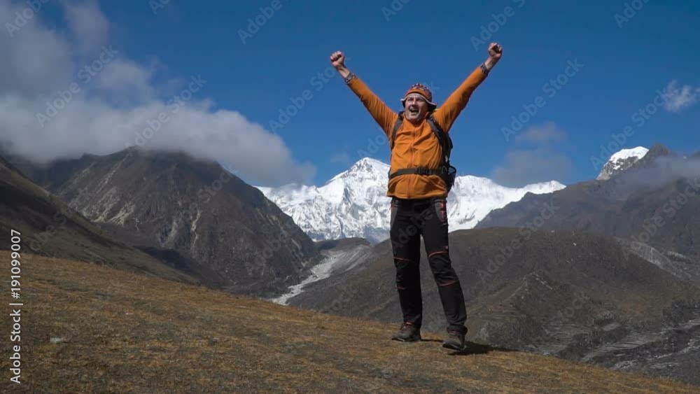 A tourist with a backpack reached the summit in the Himalayas. He is happy with his victory. Adventure and travel concept. Slow motion A tourist with a backpack reached the summit in the Himalayas. He is happy with his victory. Adventure and travel concept. Slow motion