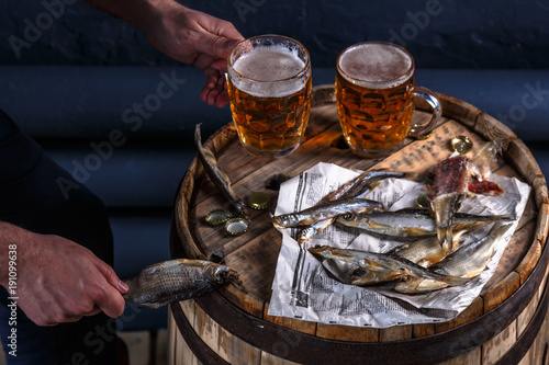 Beer mugs with dried fishes on a wooden barrel
