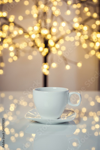 Hot tasty coffee cup on the table with background of blurred holiday lights