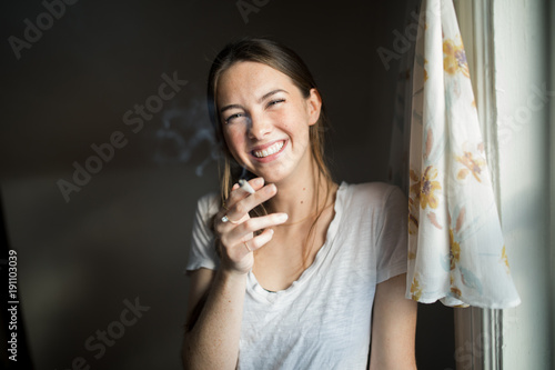 Portrait of a smiling woman smoking a joint while standing indoors