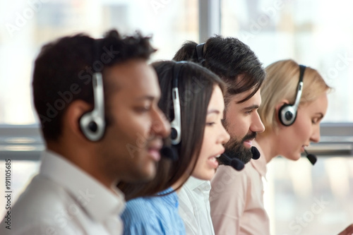 Bearded caucasian man working in call center amoung colleagues. Young bearded male employee working with a headset and accompanied by his team.