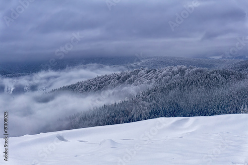 Winter foggy mountain landscape. Fairytale evening or afternoon with dramatic clouds in the sky