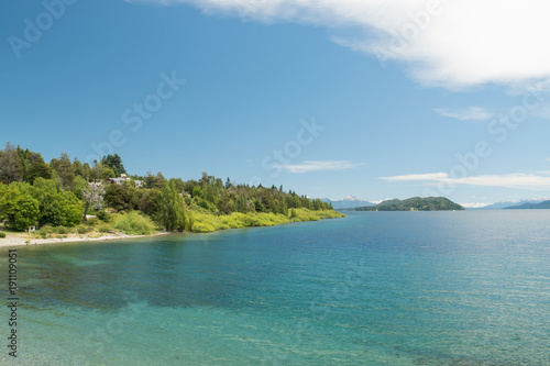 Fototapeta Naklejka Na Ścianę i Meble -  Costa frente a lago turquesa con bosque de fondo y cielo azul