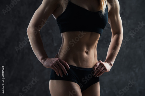 Sports sexy girl with big muscle belly in a black sportswear on a black background. A six-pack on his stomach in black color. Taut, pumped up, firm abdomen © romankosolapov