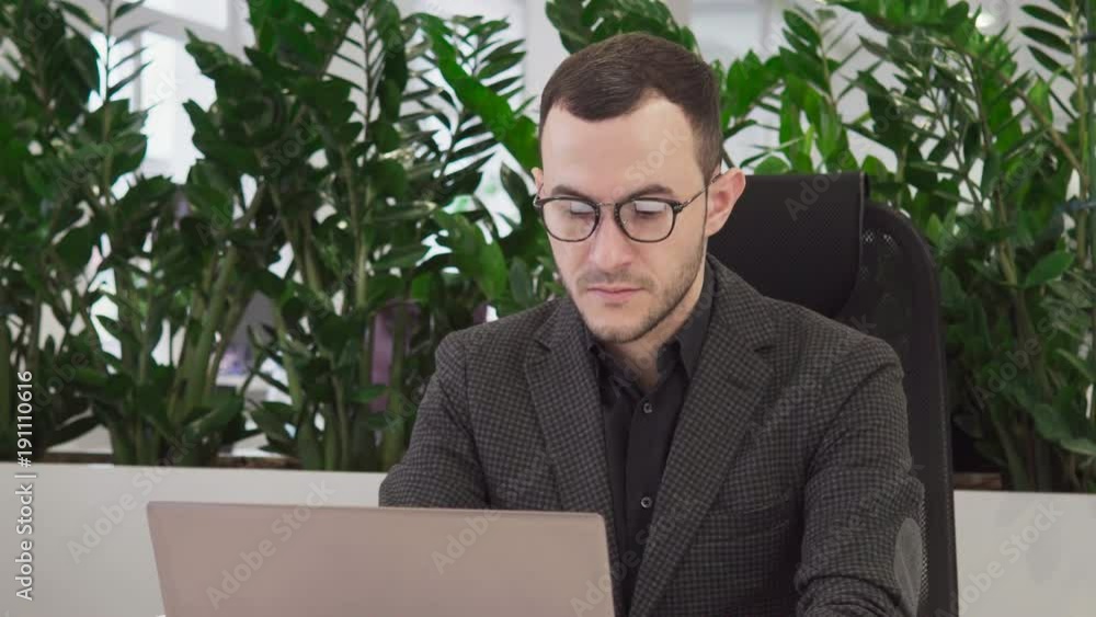 Young business man with glasses looks at the laptop screen Young business man with glasses looks at the laptop screen