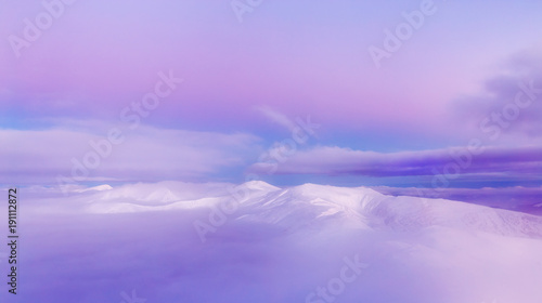 Fototapeta Naklejka Na Ścianę i Meble -  Morning clouds over snow capped mountains. Dawn scenery in pink tone. Winter season, endless snow slopes.