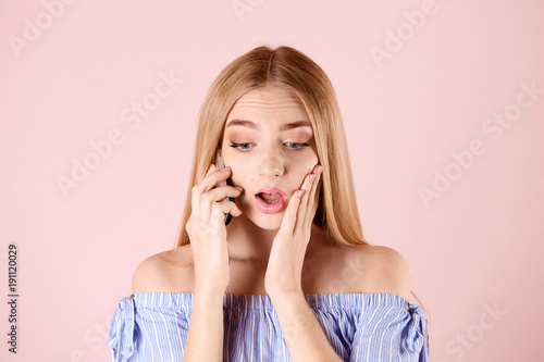 Young woman talking on cell phone against color background