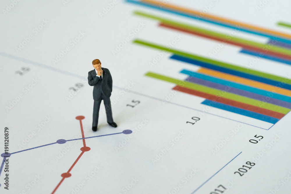 Business yearly performance review concept, miniature people figure businessman standing and thinking on printed analysis chart or graph infographic Business yearly performance review concept, miniature people figure businessman standing and thinking on printed analysis chart or graph infographic