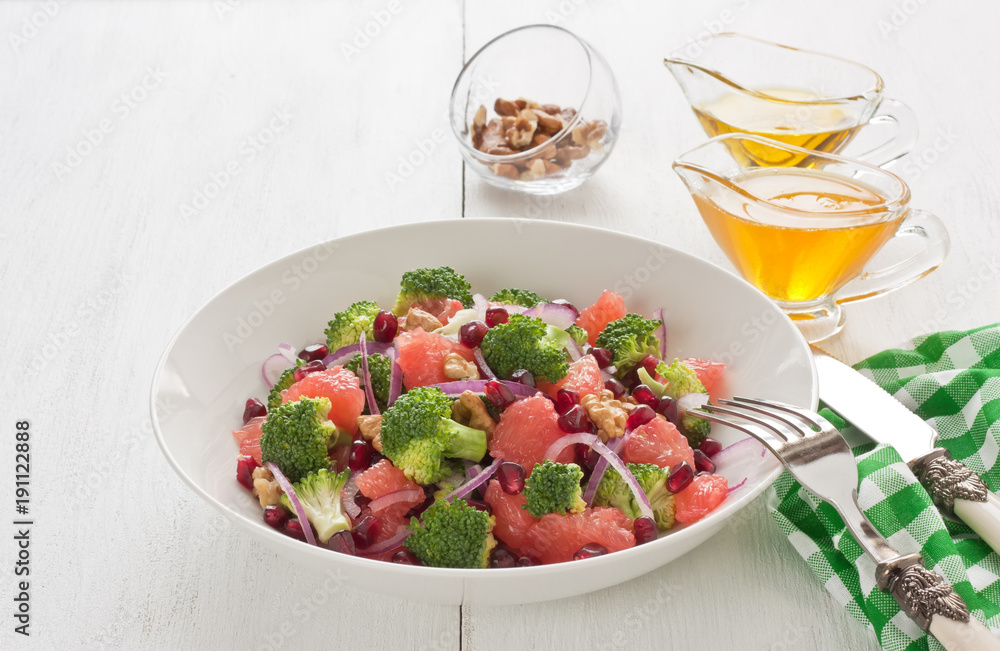 Broccoli salad / Broccoli, pomegranate, grapefruit salad with walnut, red onion, honey and olive oil in porcelain bowl on white wooden background Broccoli salad / Broccoli, pomegranate, grapefruit salad with walnut, red onion, honey and olive oil in porcelain bowl on white wooden background