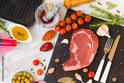 A fresh raw beef entrecote with ingredients to cooking tasty dinner, red wine and wine glasses, top view. photo