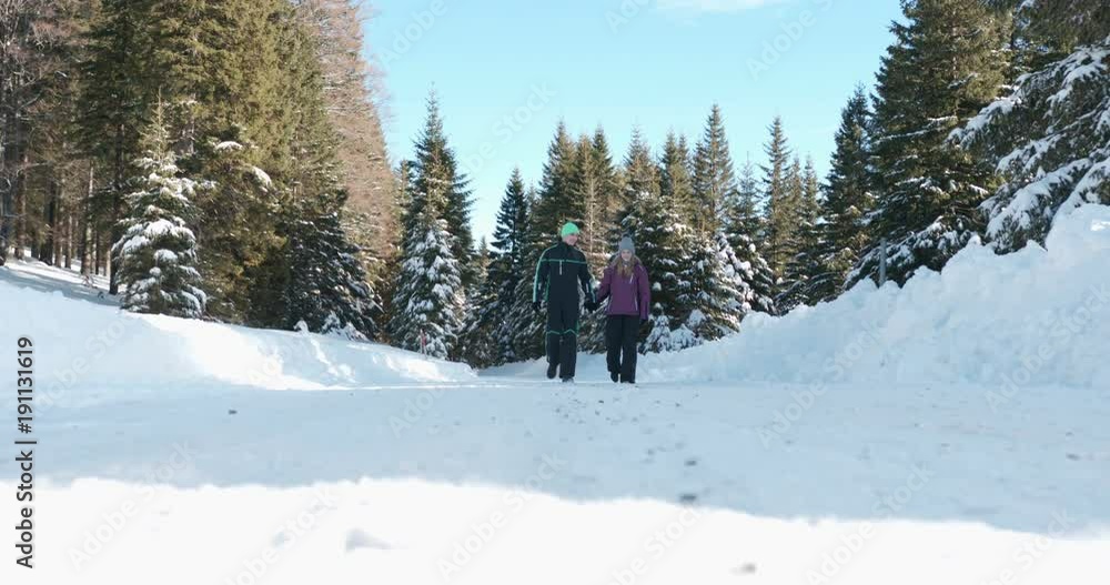 Young couple taking a leisurely walk along a snowy forest path on a beautiful sunny day Young couple taking a leisurely walk along a snowy forest path on a beautiful sunny day