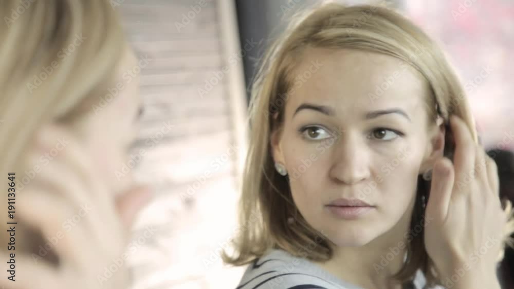 Blonde woman doing everyday makeup in front of mirror, puts powder on her cheeks with brush Blonde woman doing everyday makeup in front of mirror, puts powder on her cheeks with brush