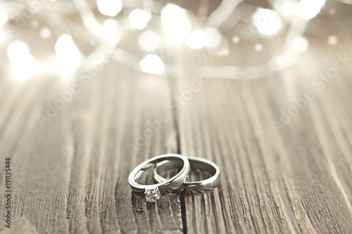 Two wedding rings place on wooden floor with light bokeh background.