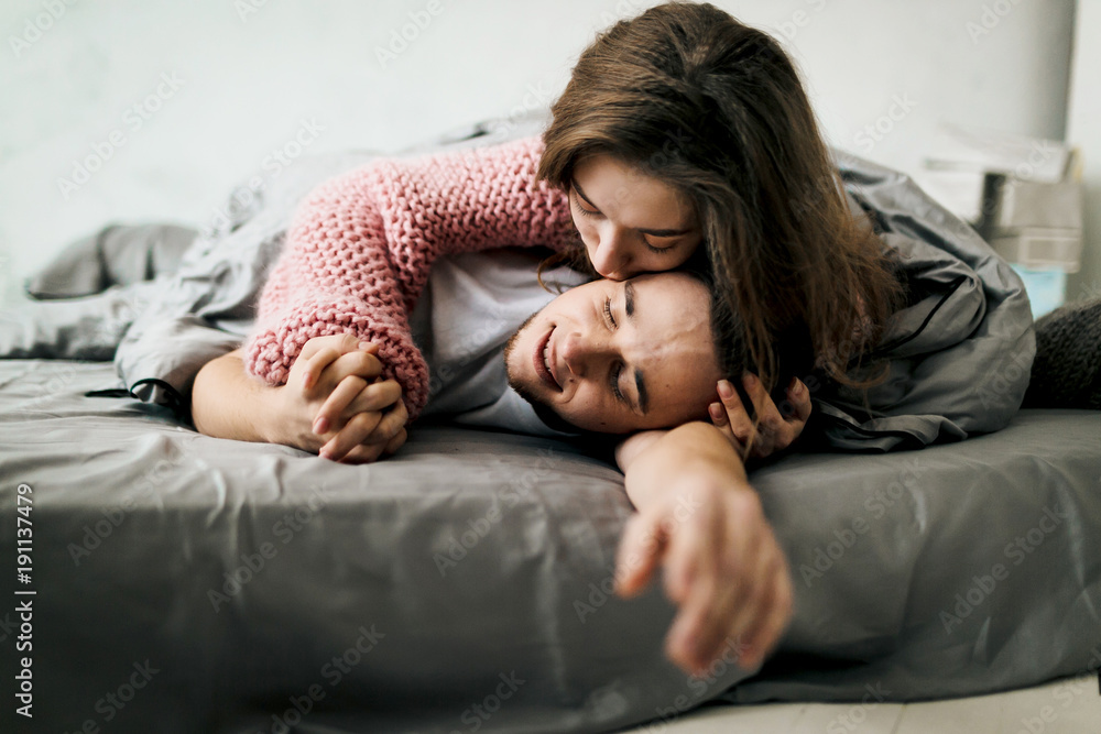 Cheerful young couple lying and hugging in bed at home. Artwork.