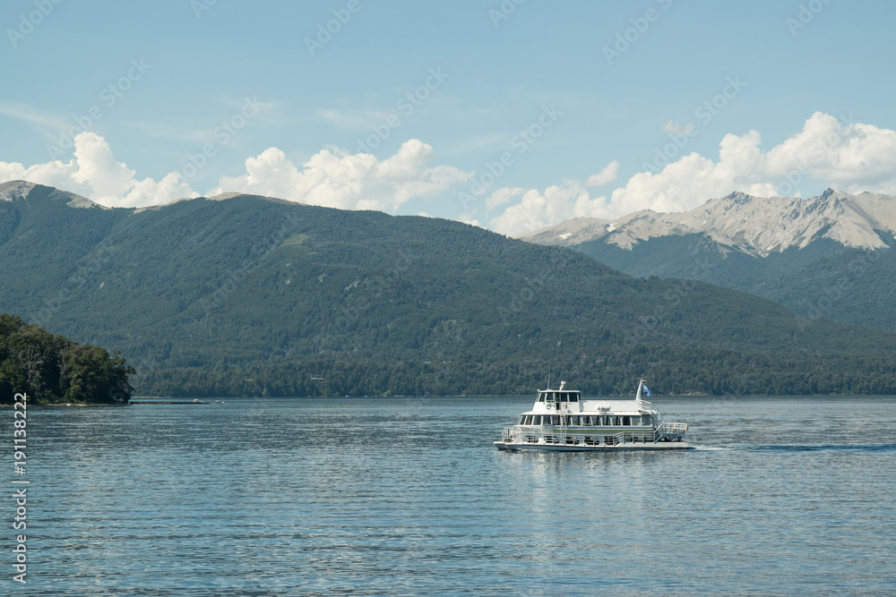 Paisaje de un lago azul con barco blanco y montañas de fondo