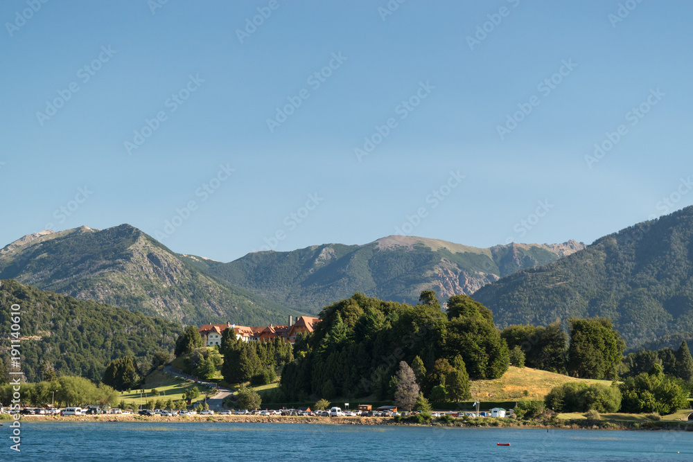 Paisaje desde el lago con hotel imponente, cielo azul y montañas de fondo