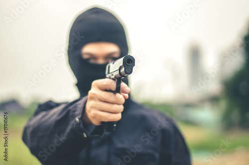 Mask thief in balaclava with holding gun ,Outlaw bad man hold a gun pointing the target , robber in black hood holding gun and pointing to victim