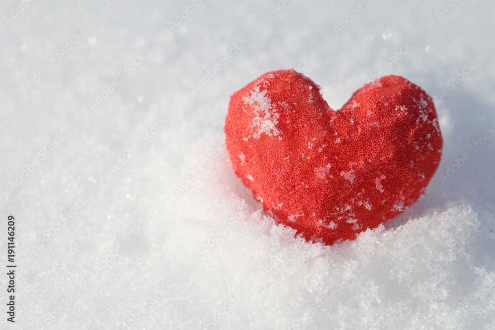 In the snow lies a red heart. A blue background for a greeting card template for Valentine's Day.