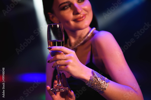 Young celebrating woman black dress, holding a glass of champagne. Party.