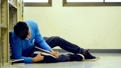 Young student study hard in library. Tired Asian male university student doing study research in library reading book on floor and yawning. For back to school education diversity concept.