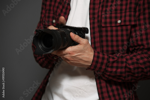 Close-up - young male photographer wearing casual clothes holding camera against a gray background