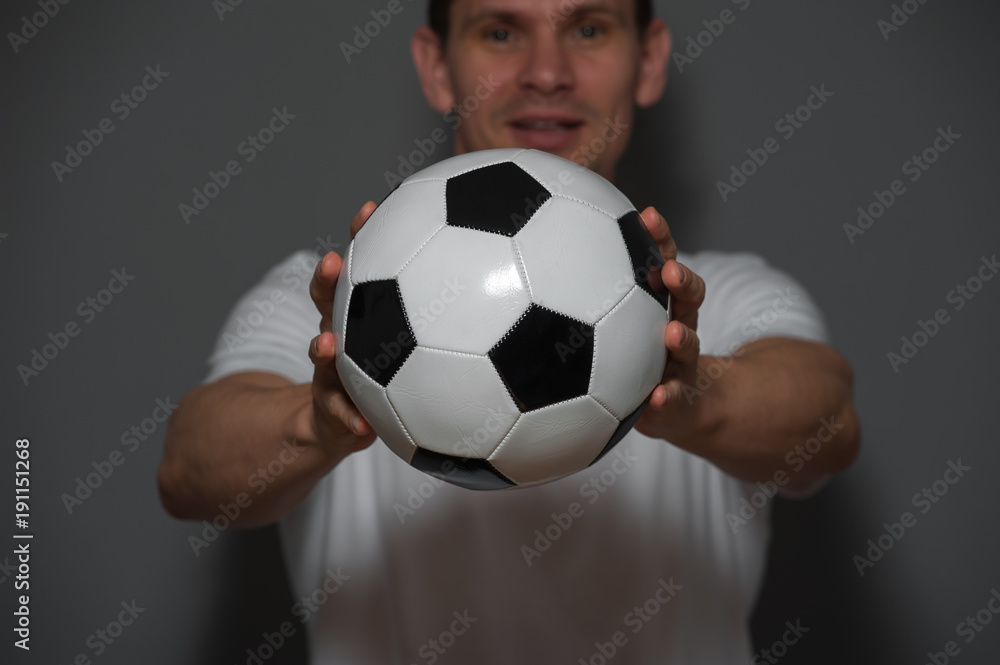Close-up - positive male soccer or football player or fan posing with ball on gray background